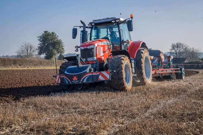 Red tractor with a front weight bumper attached, working in a field and pulling agricultural equipment