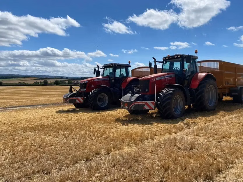Two red tractors with front weight bumpers are parked on a harvested field under a partly cloudy sky