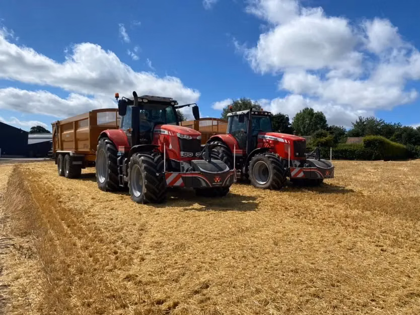 Two red tractors with front weight bumpers and LED safety boxes parked on a harvested field under a blue sky