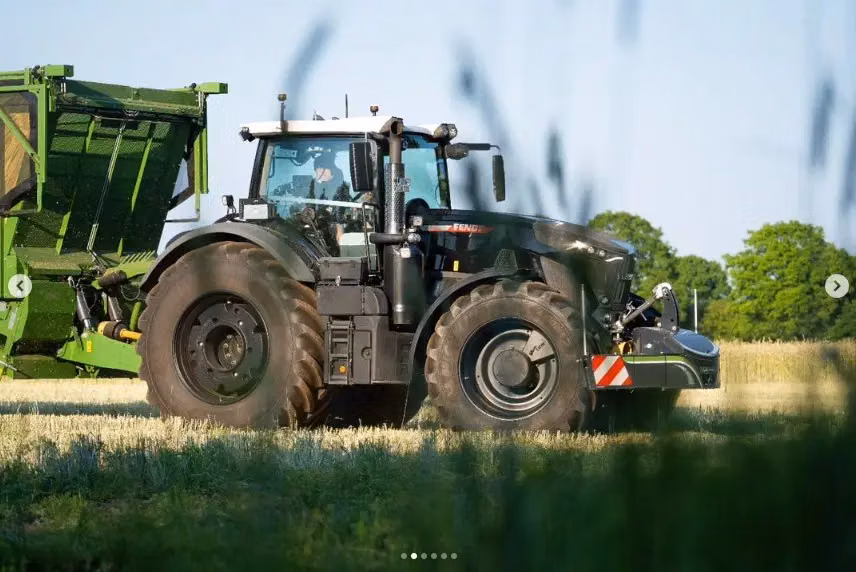 Black tractor with a front weight bumper and LED lights working in a field, towing green agricultural machinery