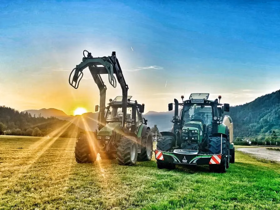 Two green tractors on grass at sunset, one with a front loader and the other with a front weight bumper attached