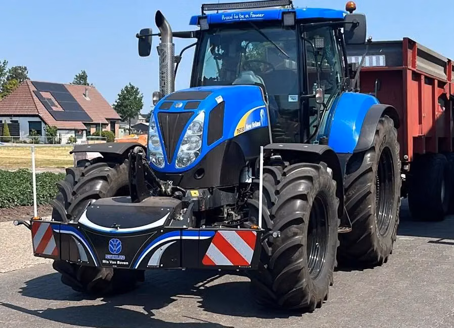 Blue tractor with large front weight bumper featuring reflective red and white stripes parked on a road