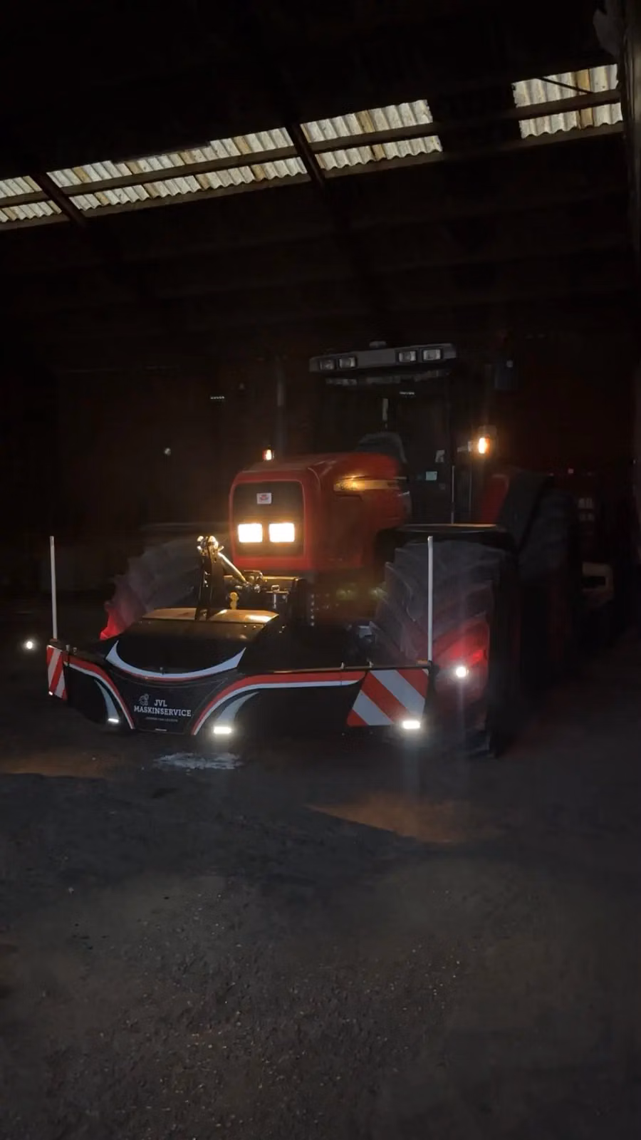 A red tractor equipped with a front weight bumper featuring LED lights and reflective safety markings indoors