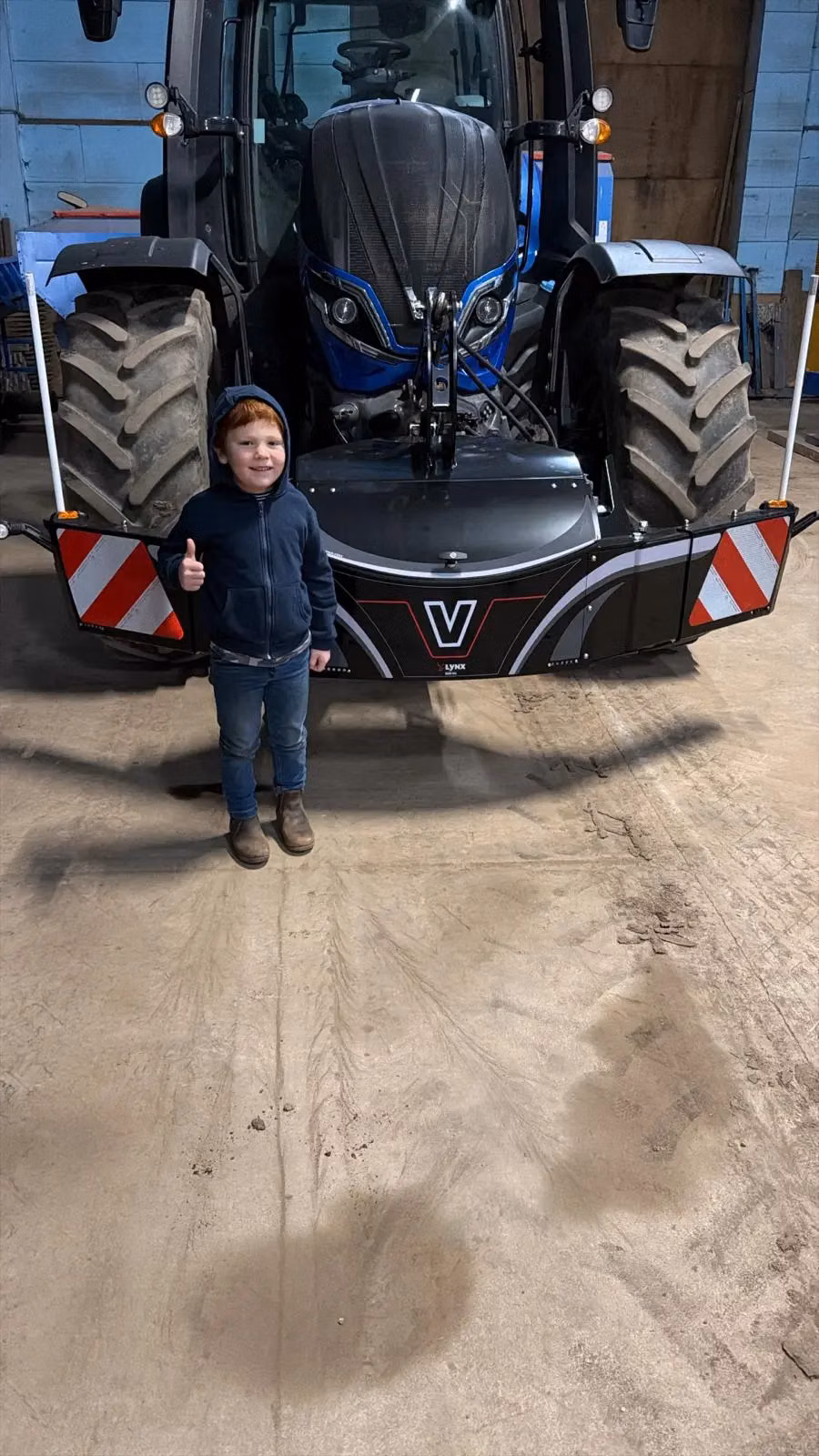 A child standing in front of a tractor with a front weight bumper displaying warning stripes and a V logo