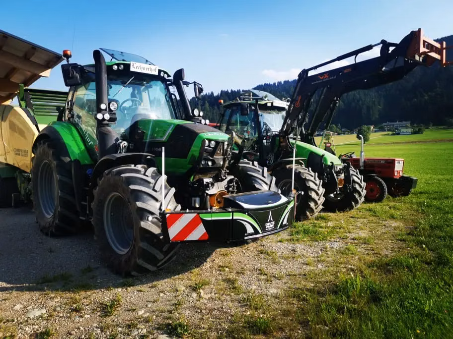 Two green tractors equipped with front weight bumpers are parked on grass beside farm equipment.