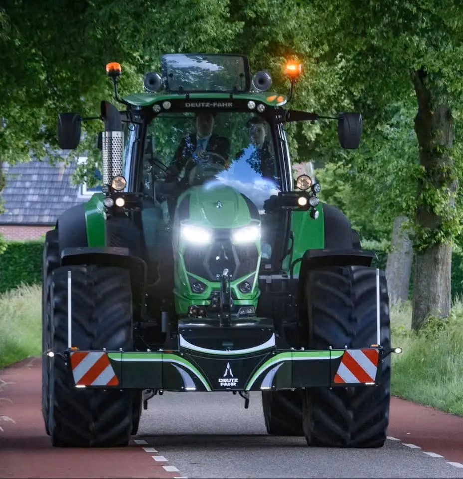Green tractor with front weight bumper featuring Deutz-Fahr branding and reflective safety markings on a road