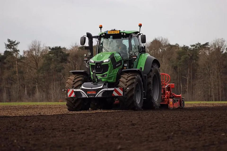 A green tractor with a mounted front weight bumper and red rear equipment working in a plowed field