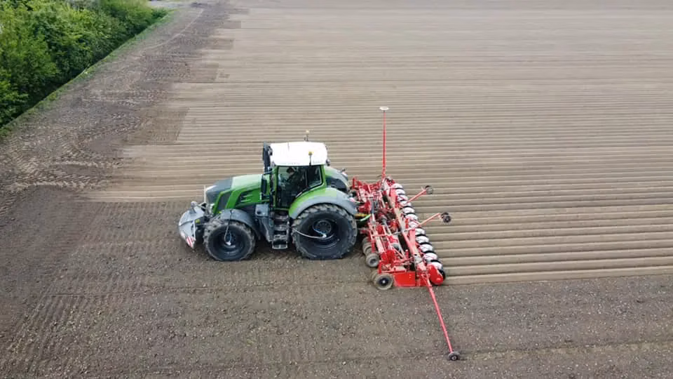 Green tractor with a front weight bumper pulling red agricultural equipment across a freshly tilled field