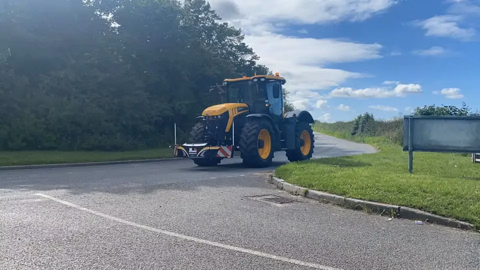 Yellow and black tractor with a front weight bumper featuring LED lights parked on a paved road near greenery