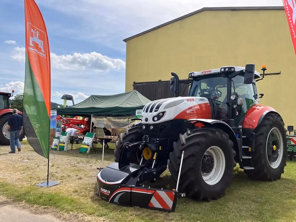 A large tractor with a mounted front weight bumper featuring reflective stripes is displayed at an outdoor event