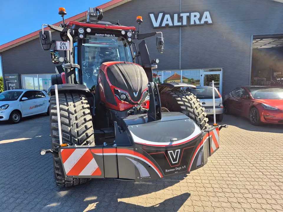Red tractor parked outside with a large front weight bumper featuring reflective stripes and LED lights attached