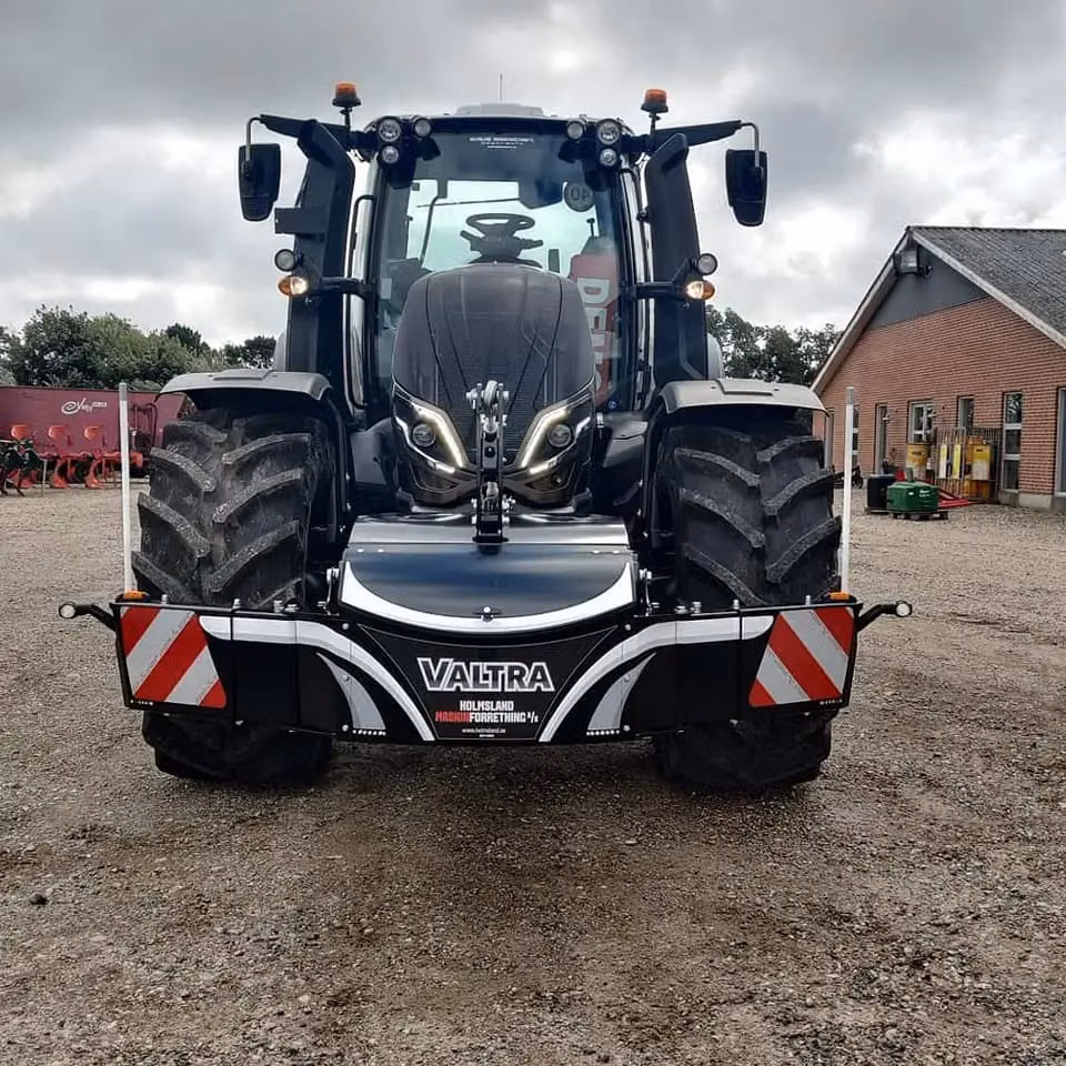 A black tractor with a front weight bumper displaying the word Valtra and red and white warning stripes.